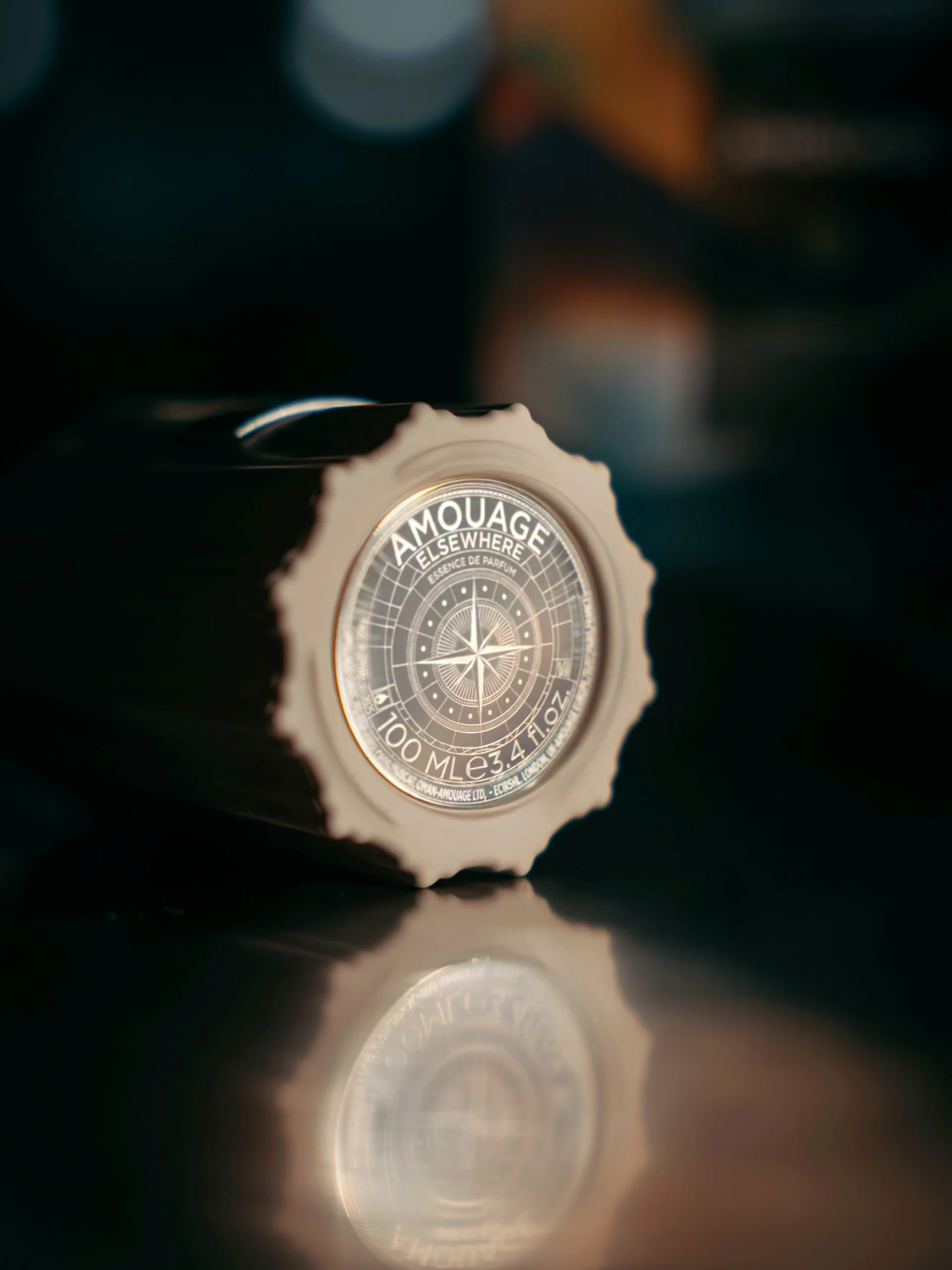 An Amouage bottle seal reflected in a dark surface